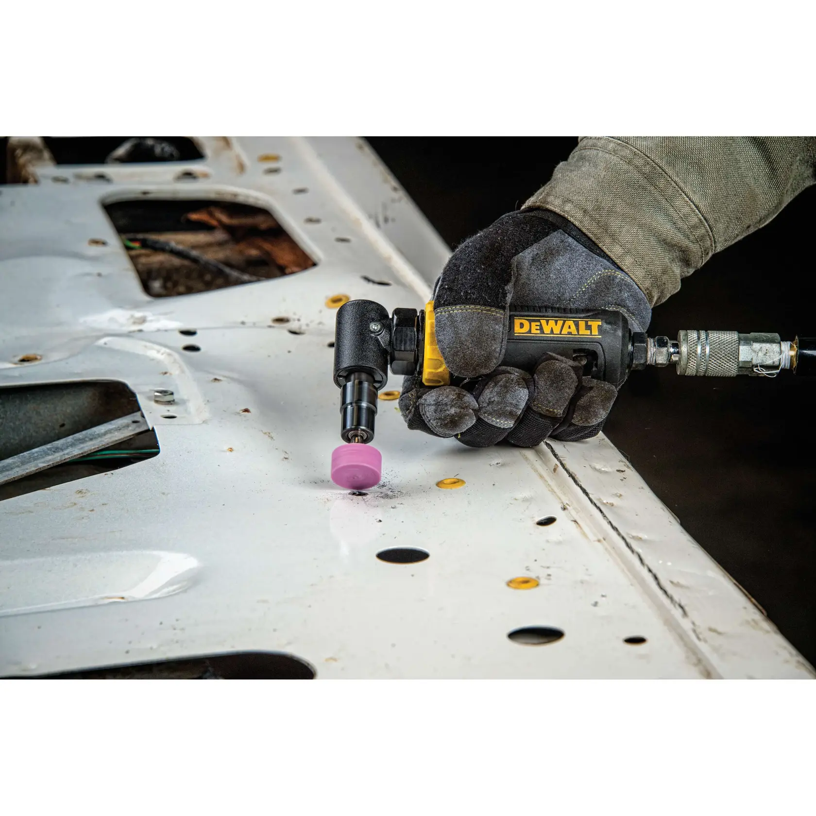 A person wearing work gloves uses a DEWALT pneumatic angle die grinder with a pink abrasive attachment to grind or polish a metal surface.
