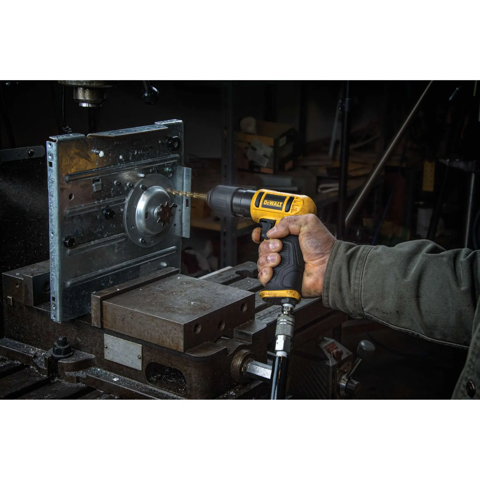A person is using a yellow and black DEWALT pneumatic drill to make a hole in a metal industrial part, inside a workshop.