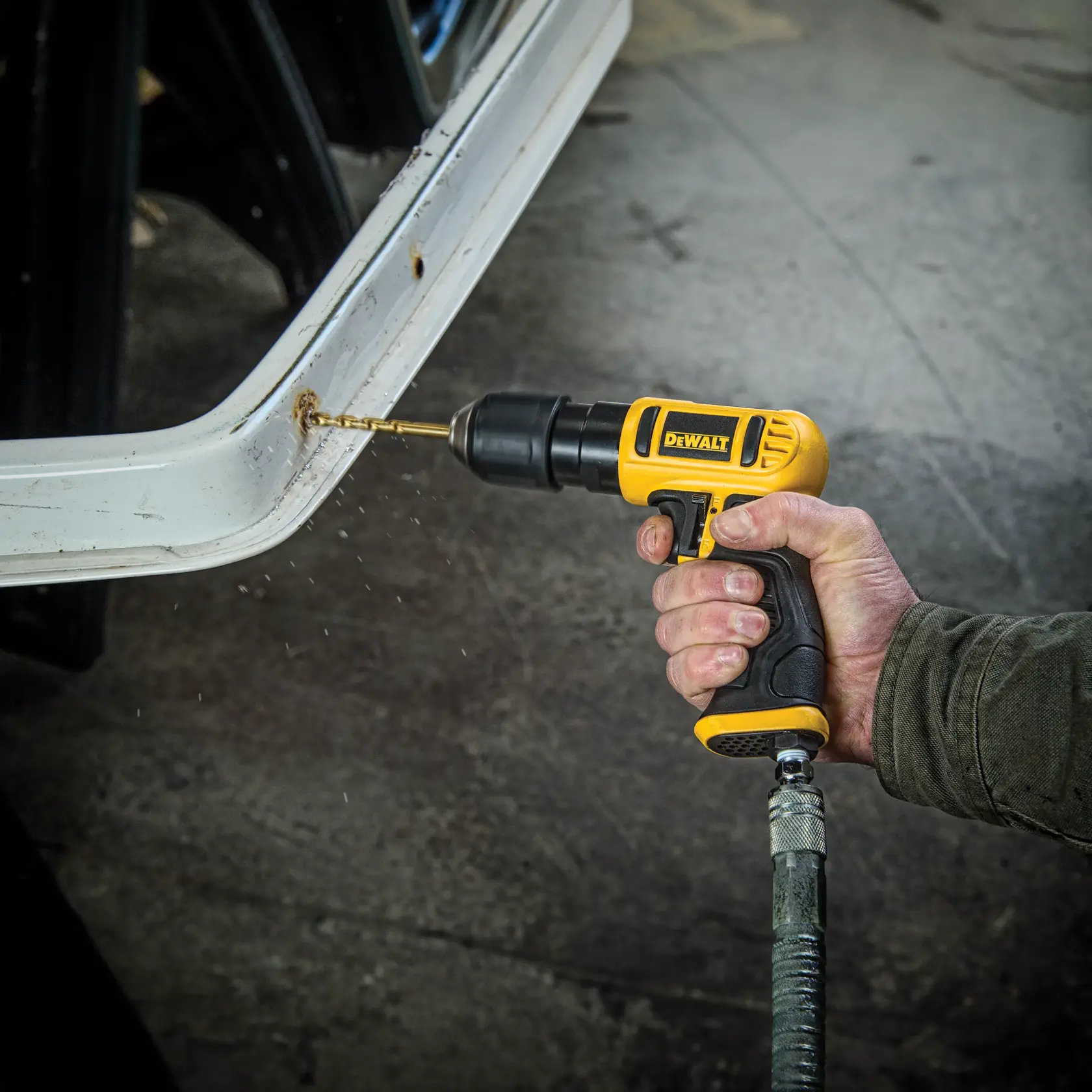 A person using a DEWALT pneumatic drill to drill a hole into a white metal surface, with metal shavings visible.