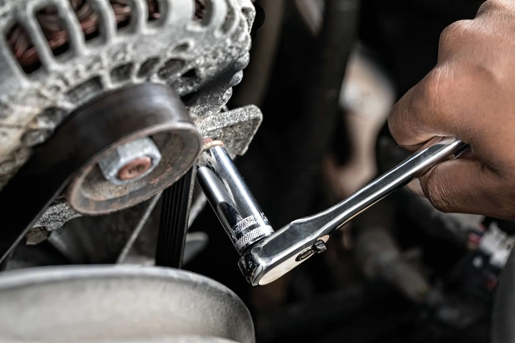 A hand using a DEWALT ratchet wrench to tighten or loosen a bolt on an engine component in a vehicle.