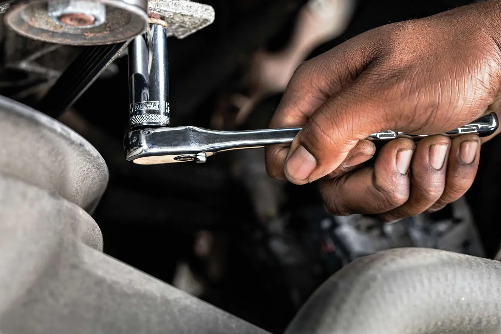 A person’s hand using a DEWALT ratchet wrench to tighten a bolt on machinery.