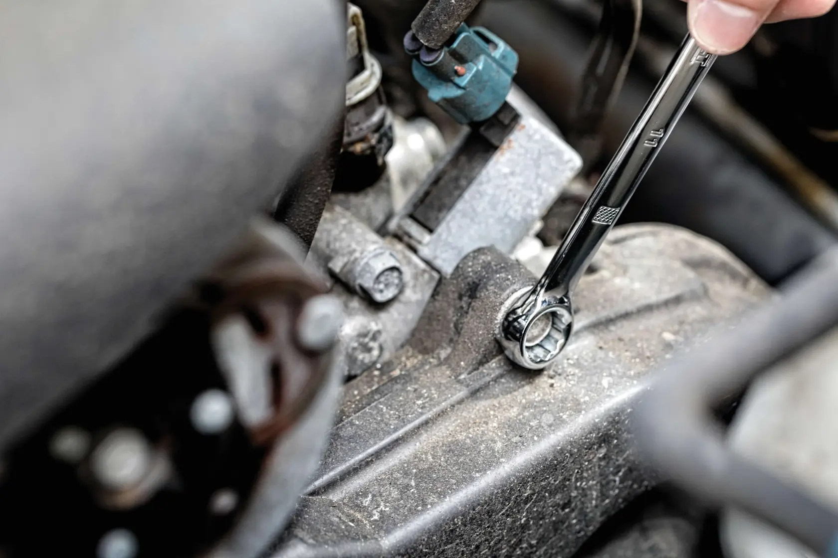 A close-up view of a hand using a combination wrench to tighten or loosen a bolt on an engine or machinery part.