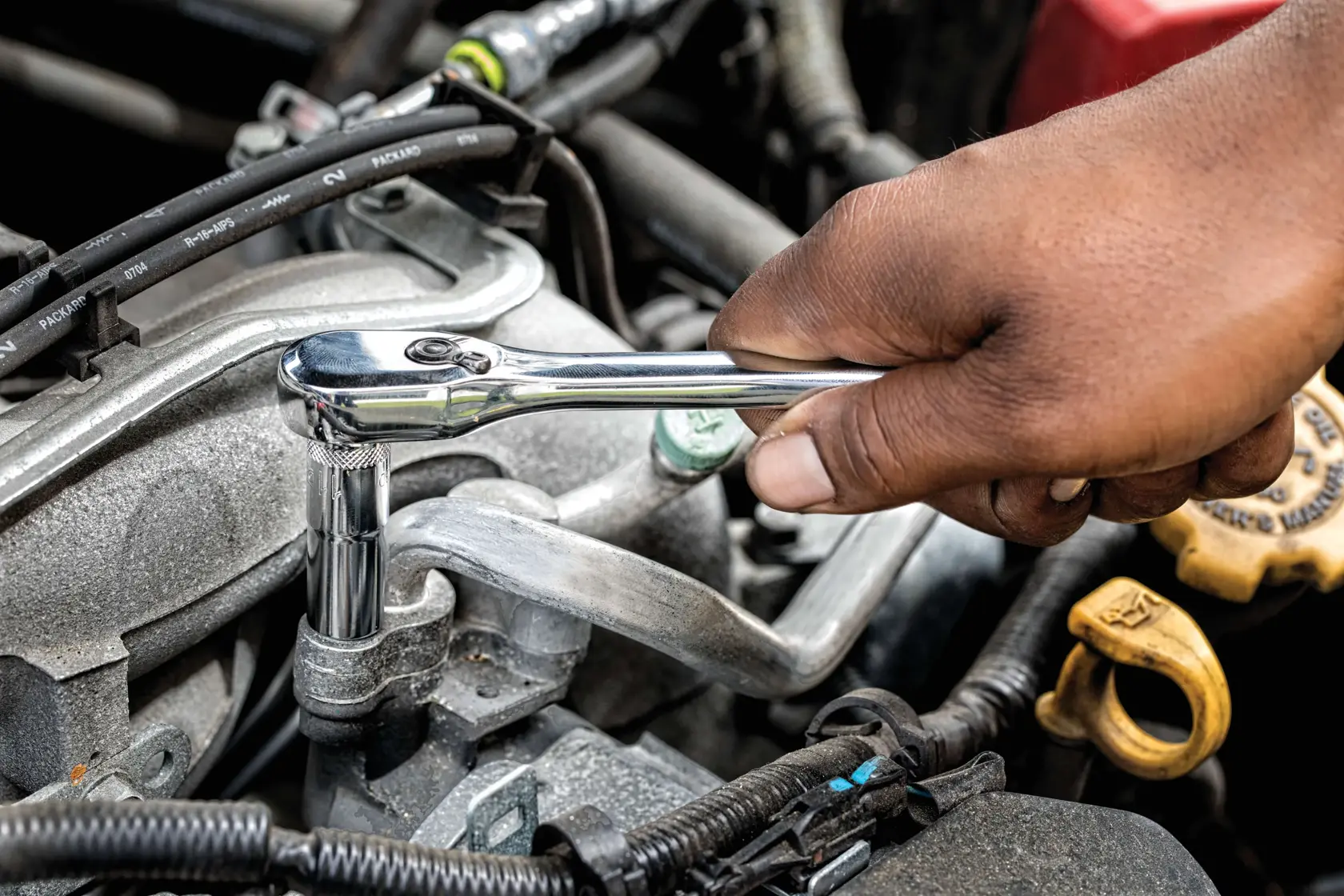A close-up of a hand using a shiny ratchet wrench to work on a car engine.