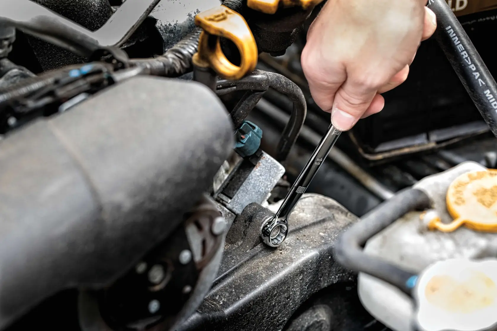 A hand using a DEWALT ratcheting wrench to tighten or loosen a bolt on a car engine.
