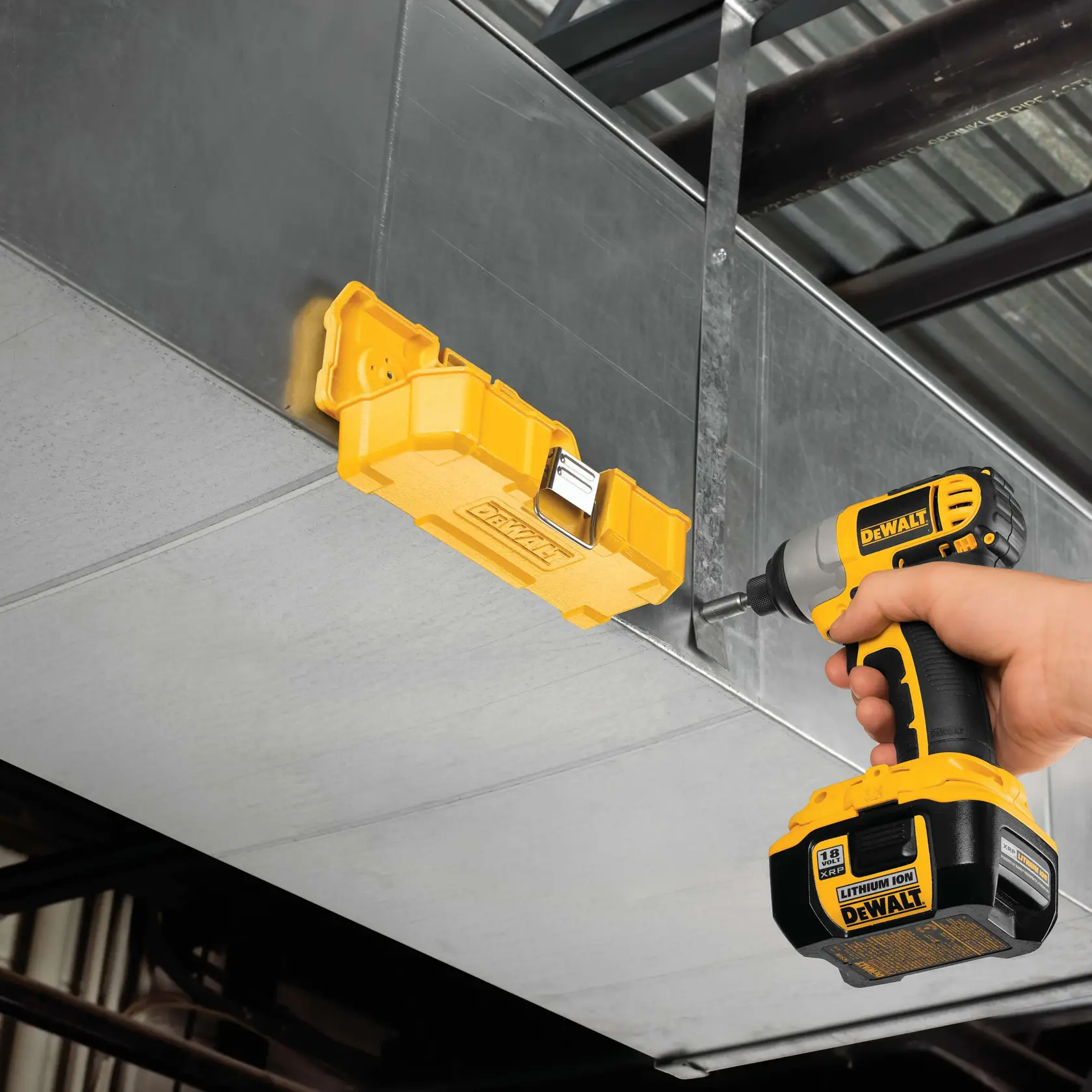 A person uses a yellow DEWALT cordless drill to attach a yellow DEWALT tool case to a metal duct or surface. The setting appears to be an industrial or construction environment.