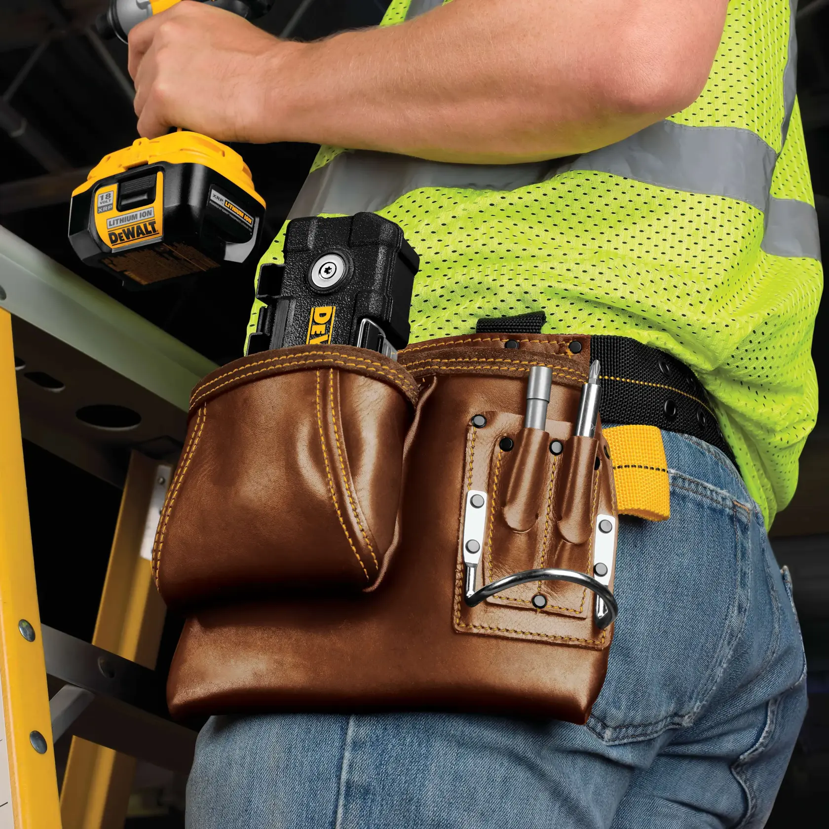 A hand holding a DEWALT cordless power tool is shown fastening a metal bracket to a large metal duct. A DEWALT branded black storage box is attached to the duct above the fastening point. The scene takes place indoors, likely at a construction site.