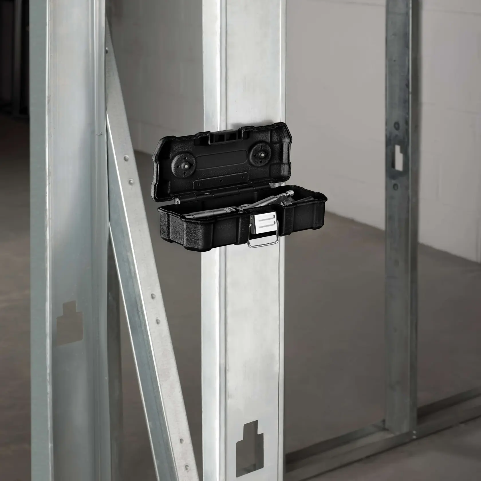 A DEWALT black plastic case containing a metal hole saw and drill bits, shown opened and placed near an electrical breaker box mounted on a wooden panel.