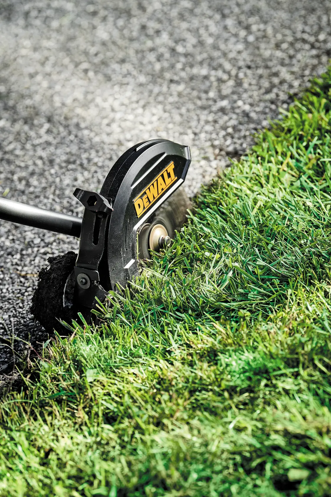 A DEWALT lawn edger attachment being used to create a clean edge between grass and pavement.