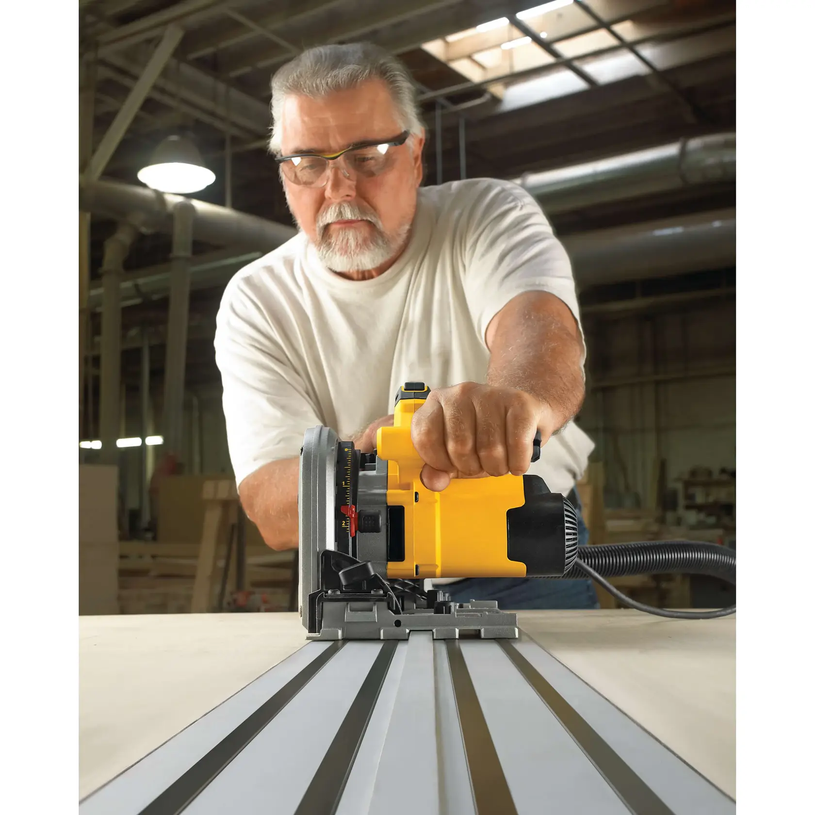 A person using a DEWALT DWS520K track saw to cut wood in an industrial workshop. The saw is guided on a metal track for precise cutting.