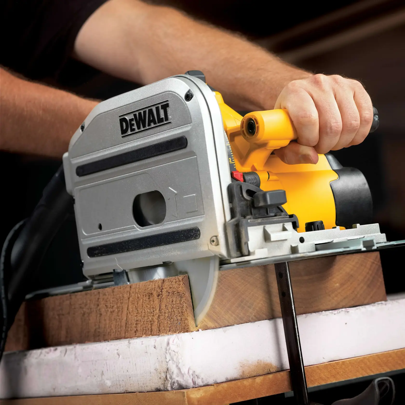 A close-up of a person using a DEWALT track saw to cut through a piece of wood. The saw is yellow and silver in color, and the blade is actively slicing through the material.