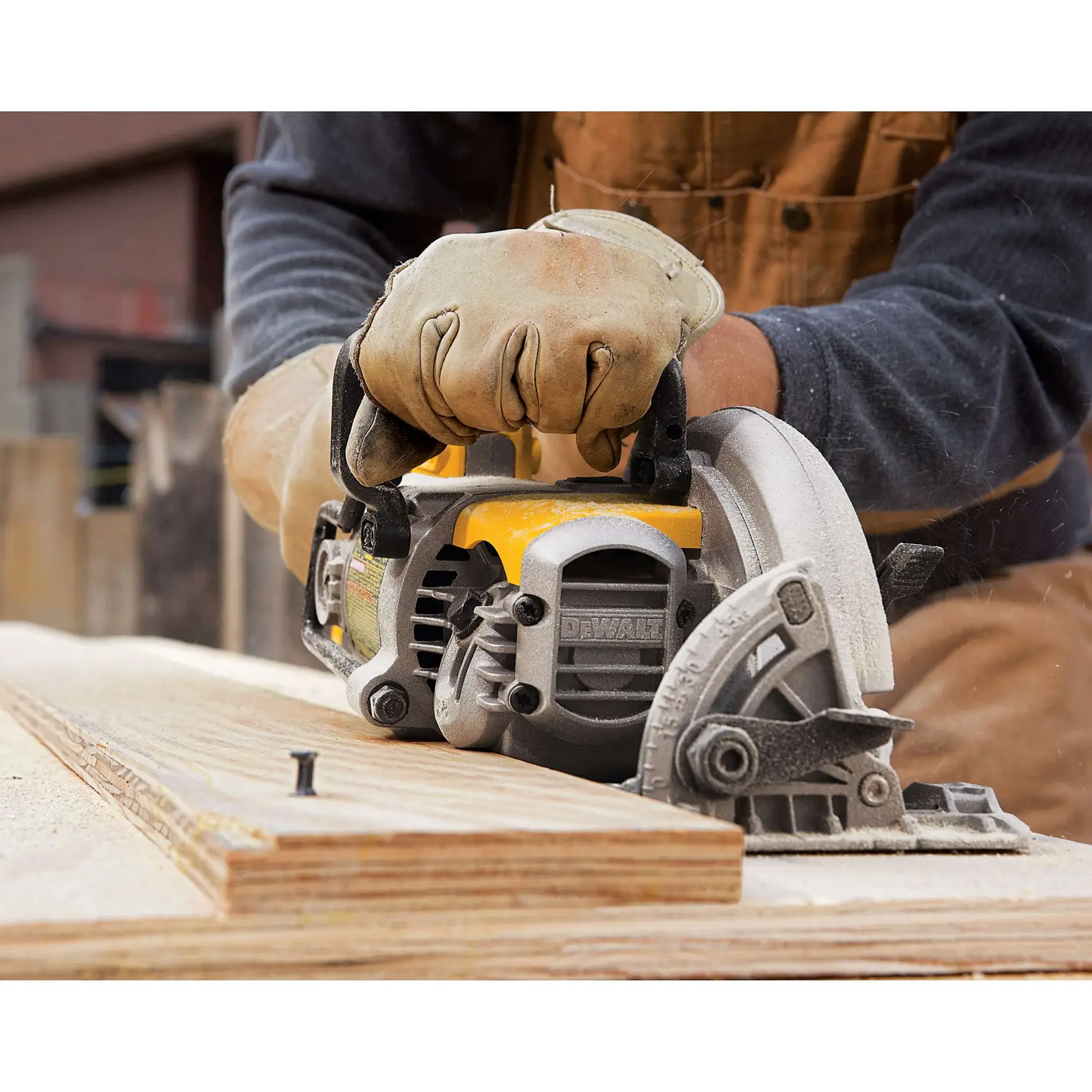 A gloved person using a DEWALT circular saw to cut a piece of plywood in a workshop setting. Sawdust is visible around the cutting area.
