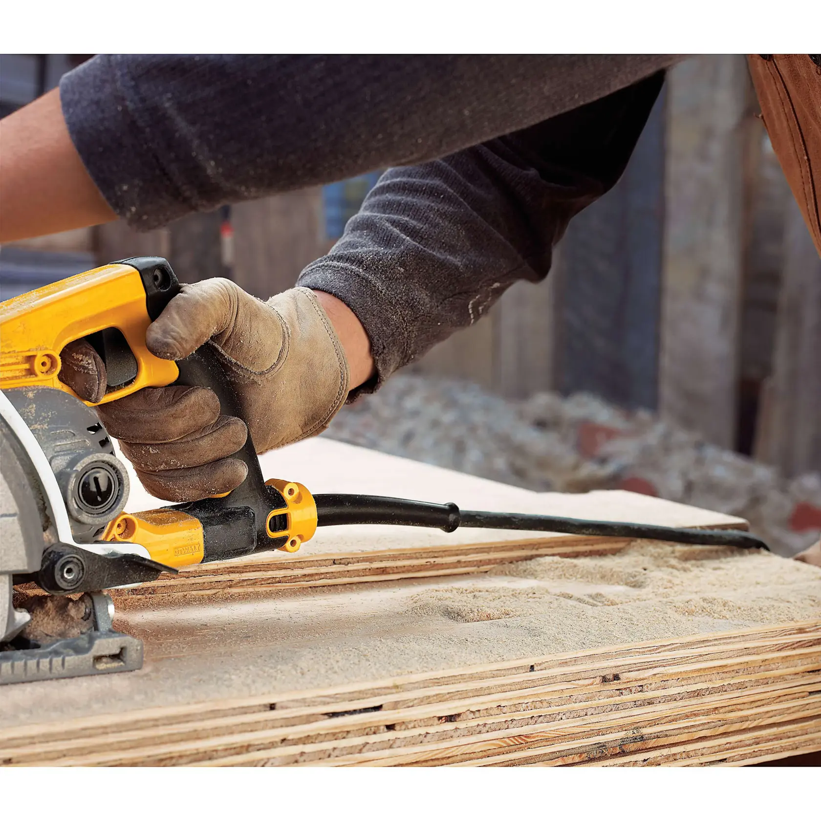 A person wearing work gloves is using a DEWALT circular saw to cut through stacked wooden boards at a construction site.