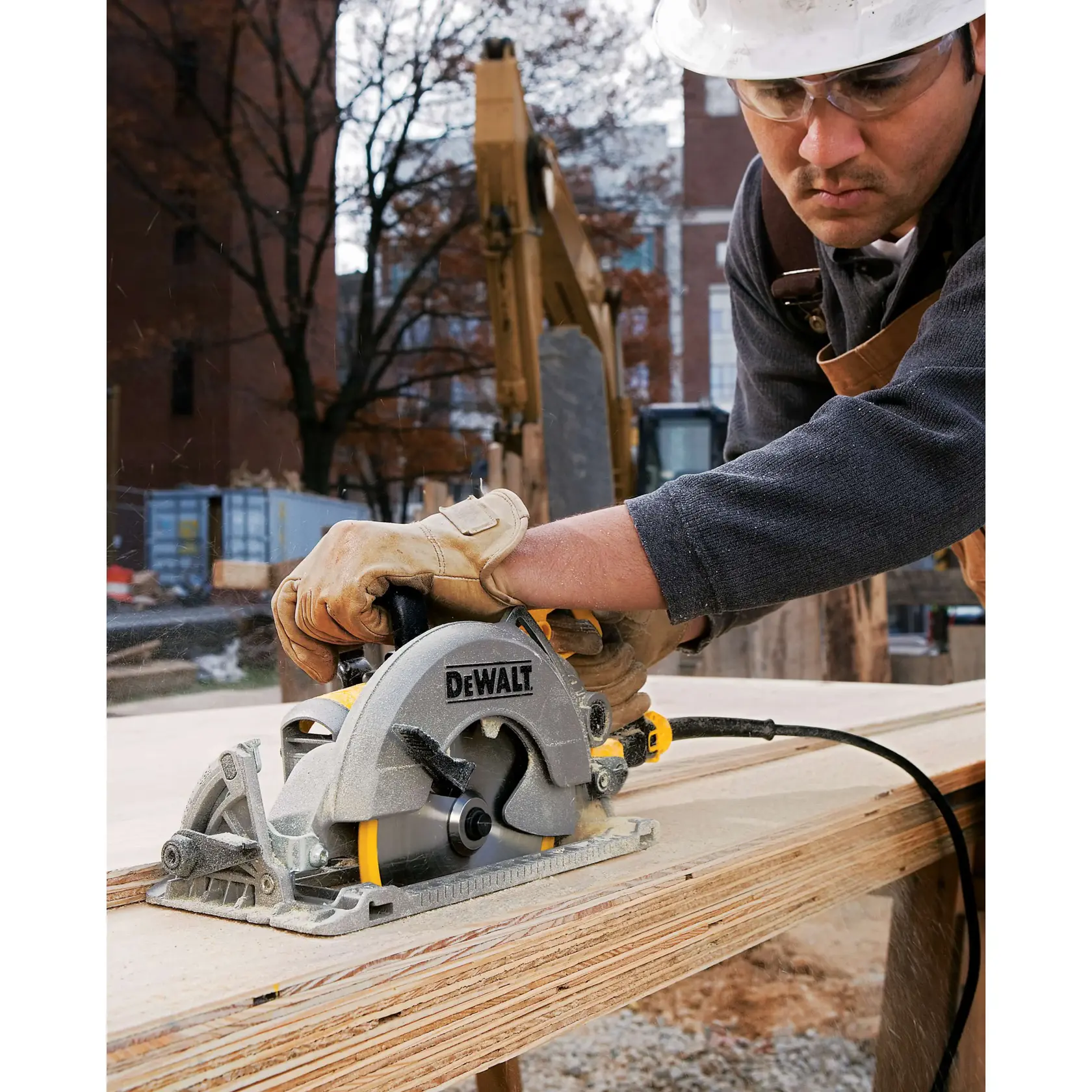 A person wearing work gloves operates a DEWALT circular saw (model DWS535B) to cut wooden boards at an outdoor construction site, with safety equipment and tools visible in the background.