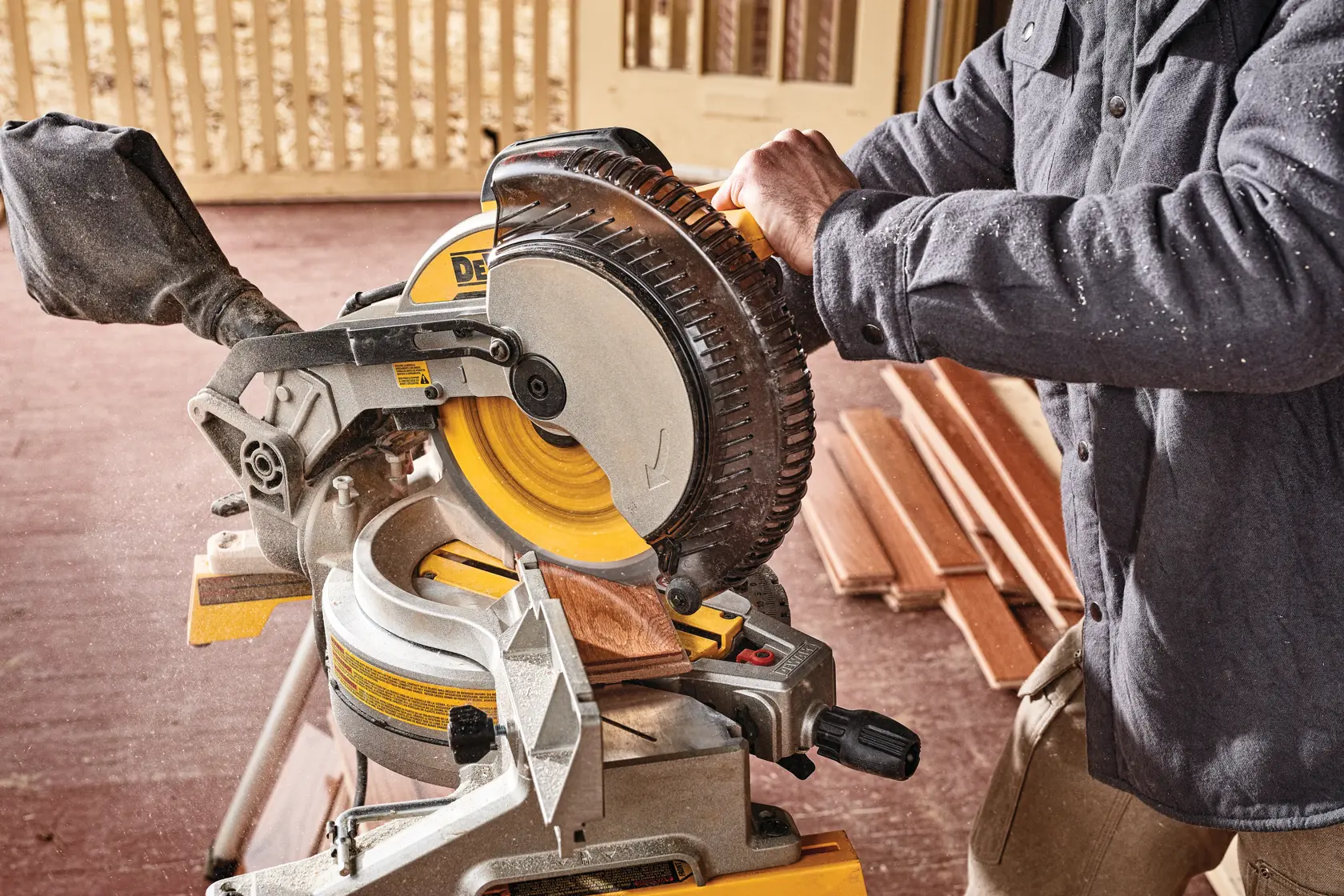 A person using a Dewalt DWS713 miter saw to cut a piece of wood, with the saw positioned on a workbench and several pieces of wood in the background.