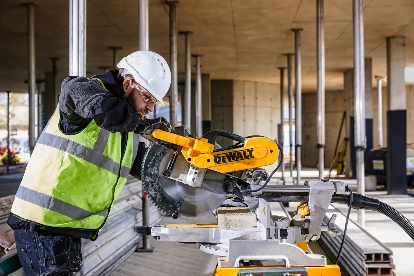 DEWALT DWS780, DWS780KIT saw in use at a construction site. Worker wears safety gear. Photography product category.