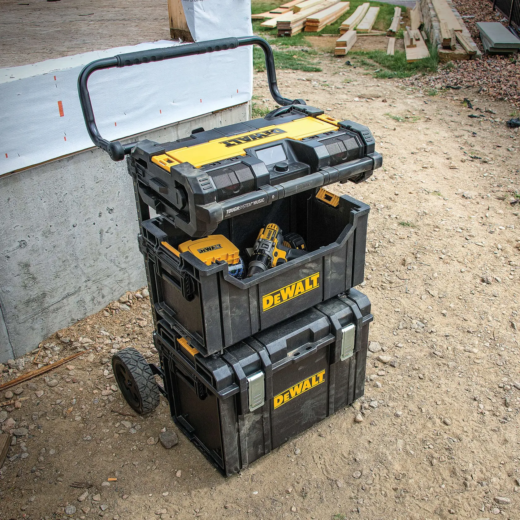 Stacked DEWALT toolboxes with a handle and wheels, positioned outdoors on a construction site, partially open to show power tools inside.