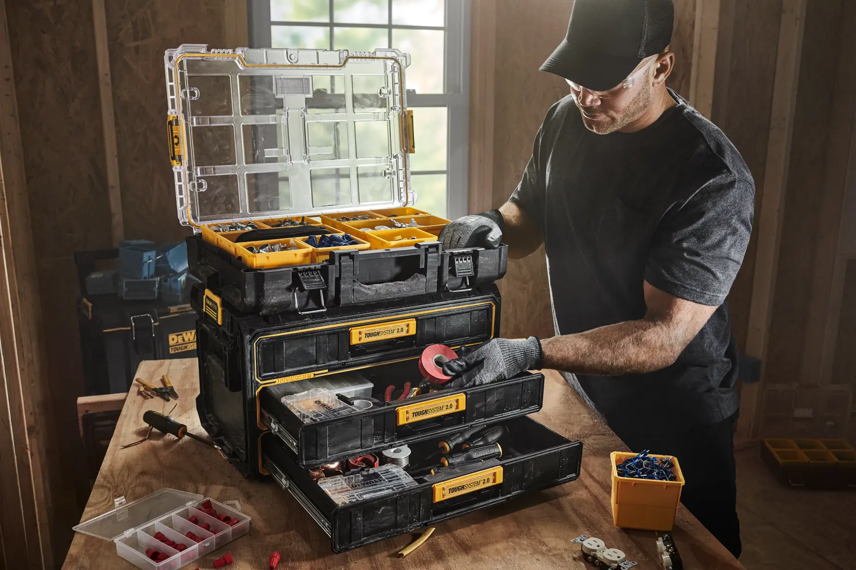 Two workers in safety gear and orange vests use DEWALT portable tool storage carts with multiple drawers on wheels inside a large construction site with concrete columns and overhead lights.