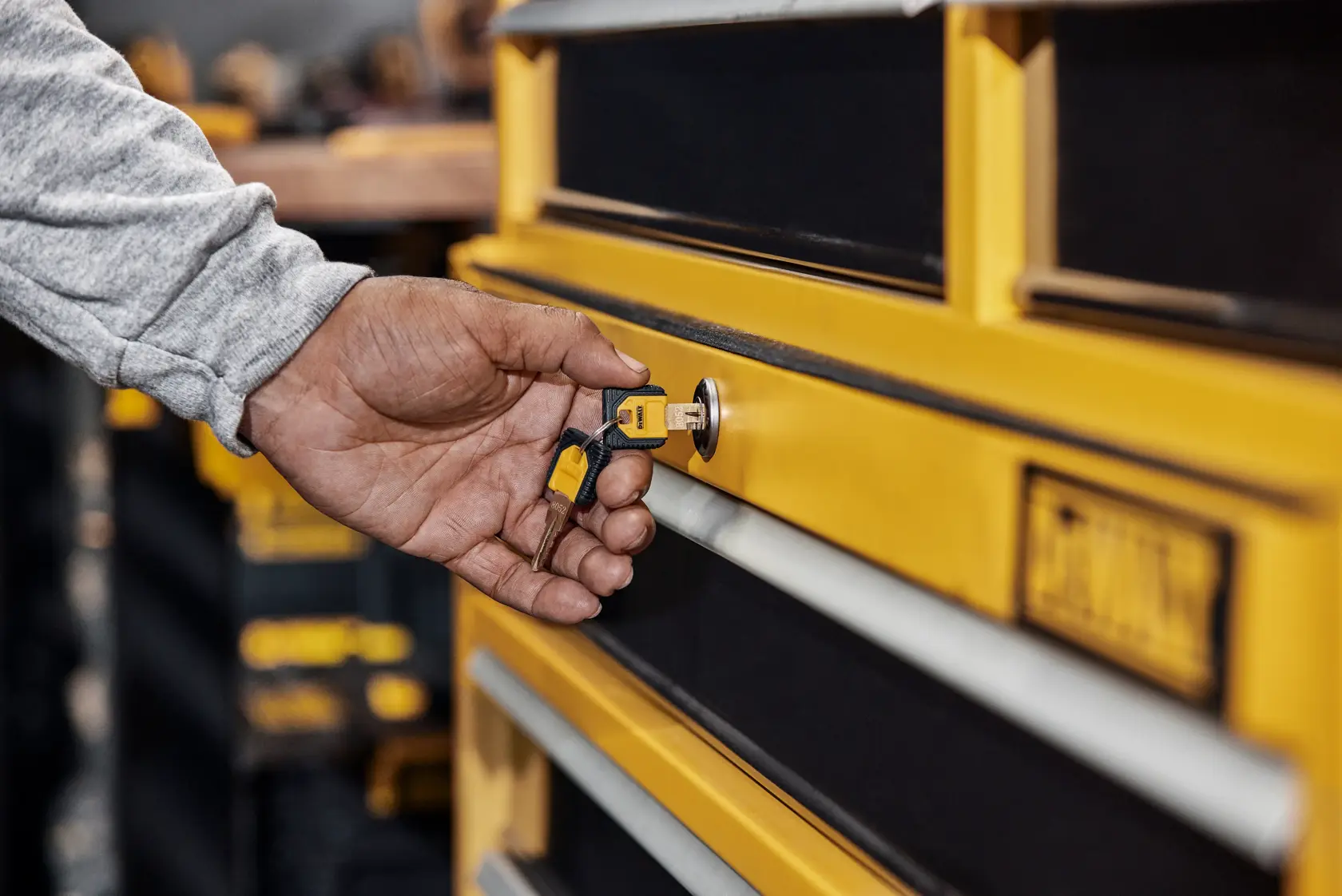 A hand is using a key to unlock or lock a yellow DEWALT tool chest drawer.