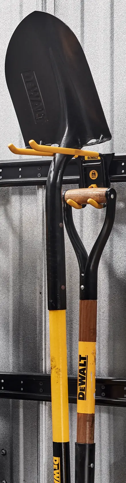 Two DEWALT shovels with yellow and black handles are mounted vertically on a metal wall rack against a corrugated metal wall.