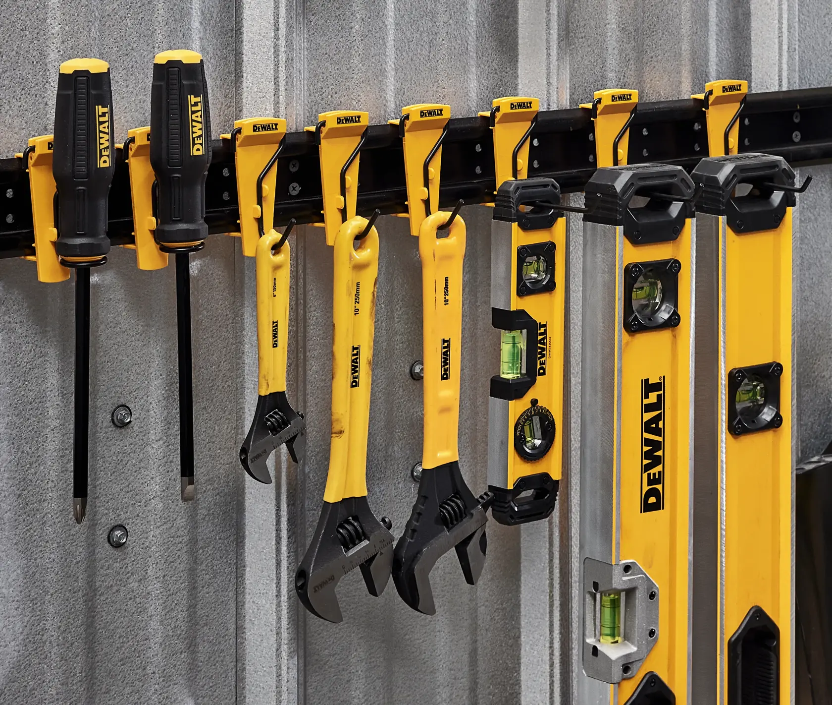 A set of DEWALT hand tools including screwdrivers, adjustable wrenches, and levels are neatly organized on a wall-mounted rack against a metal wall. The tools are yellow and black, branded with the DEWALT logo.