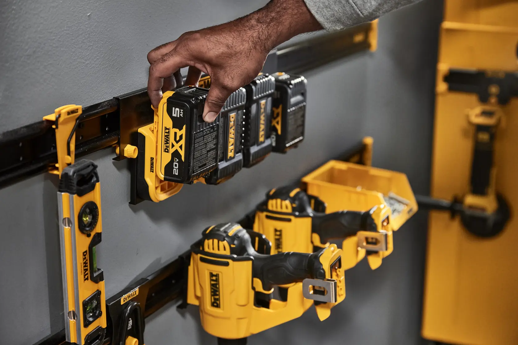 Hand placing a DEWALT XR battery onto a wall-mounted organizer with various DEWALT power tool accessories and batteries.