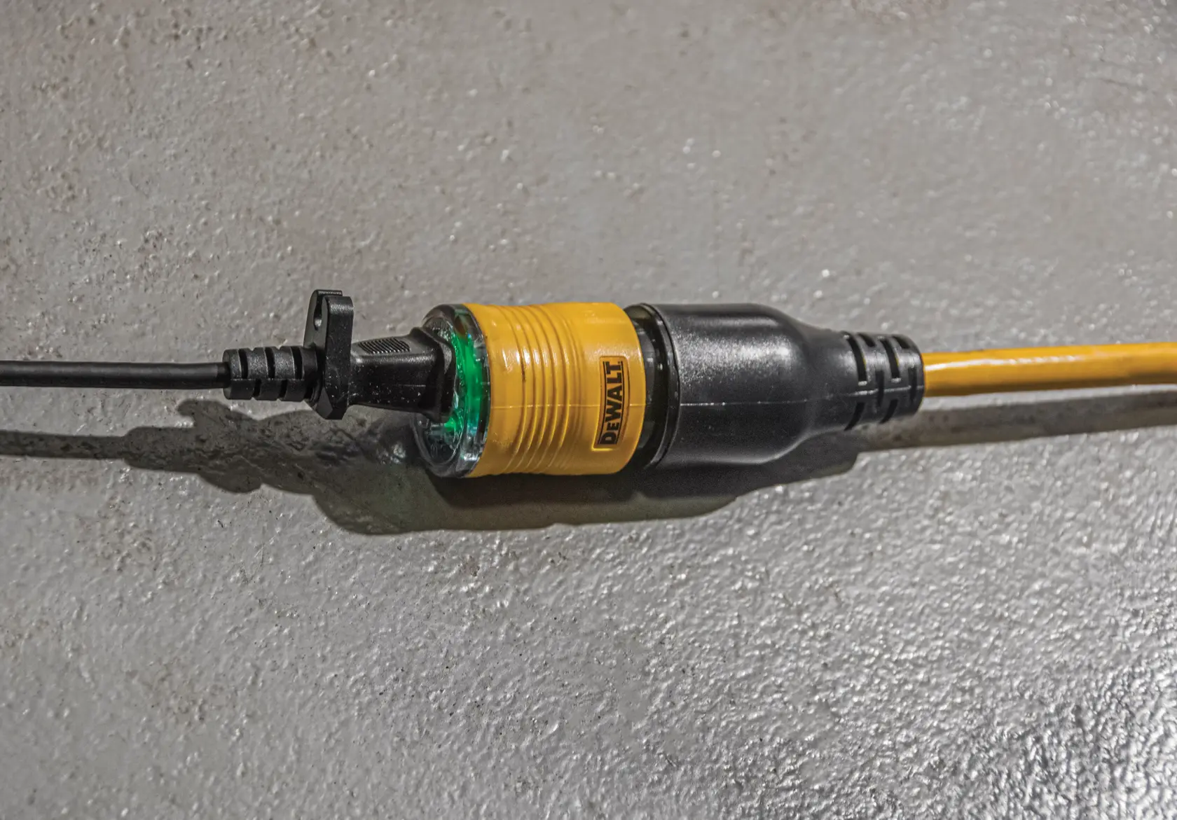 Close-up of a DEWALT extension cord with a yellow and black connector plugged into another electrical cord on a grey textured surface.
