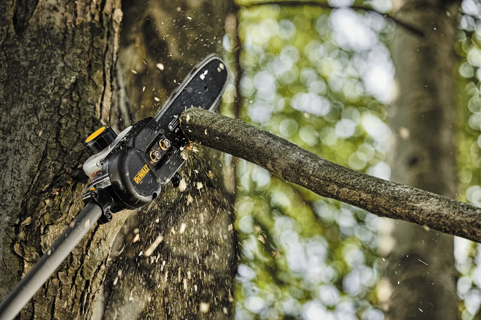 A DEWALT pole saw cutting through a tree branch, with wood chips flying. The saw is attached to an extension pole and is actively trimming a limb outdoors.