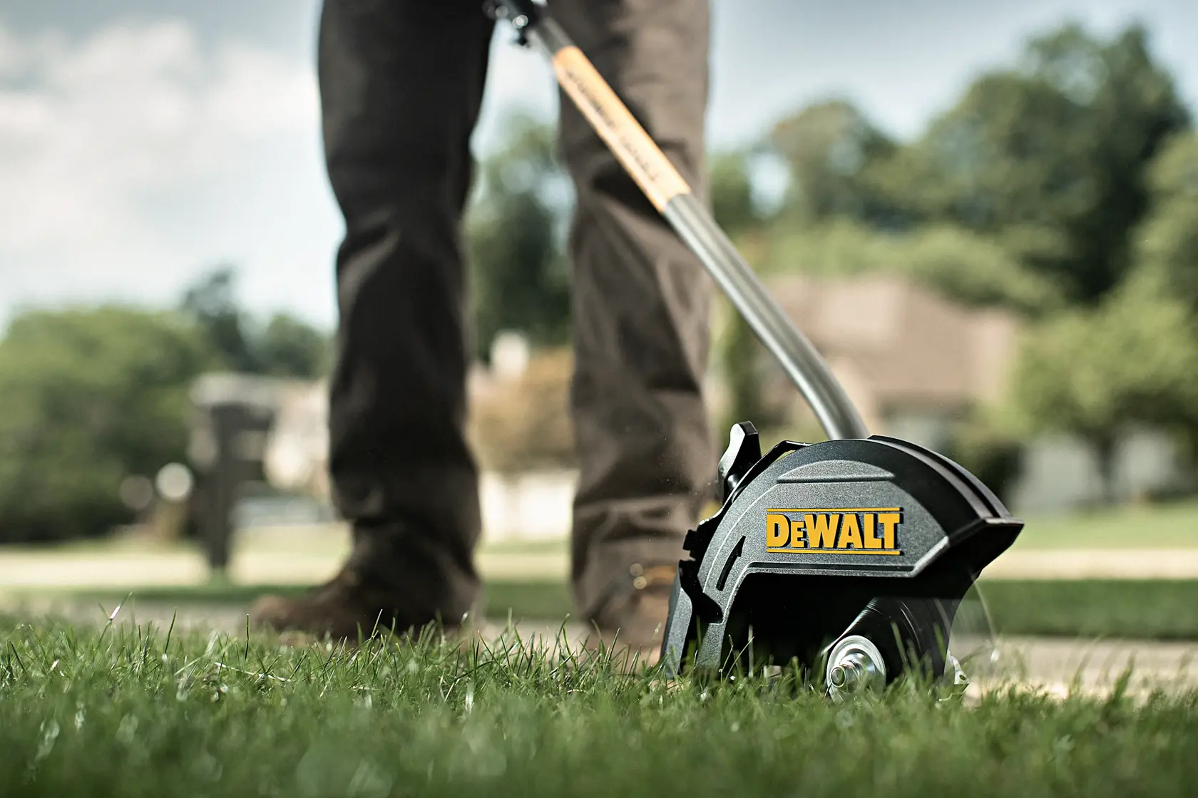 A person using a DEWALT lawn edger tool to trim the edge of a lawn, shown close-up with the tool cutting along the grass.