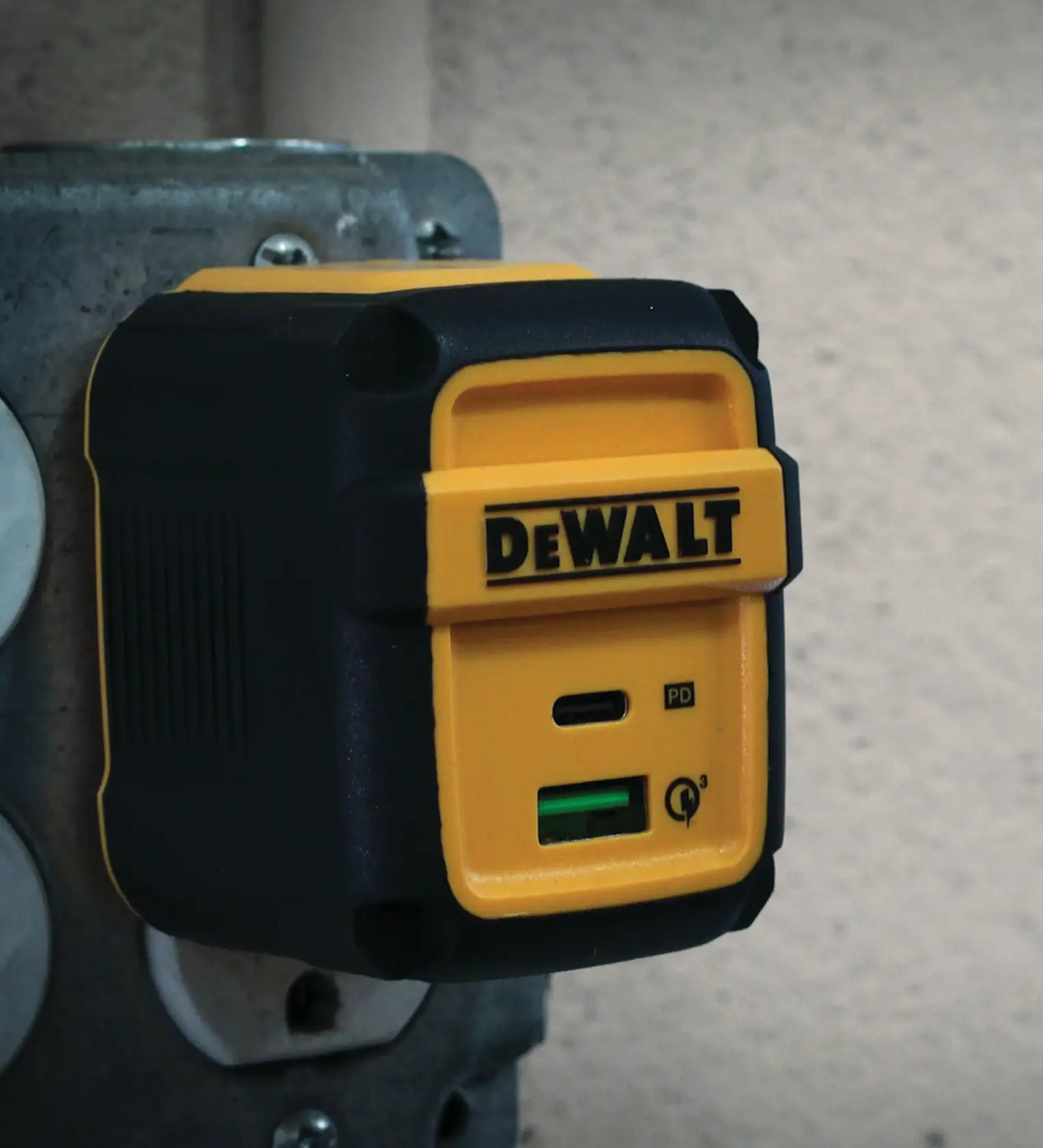 A DEWALT branded yellow and black electrical adapter is plugged into a metal outlet. The adapter has a USB-C and a USB-A port for charging devices.