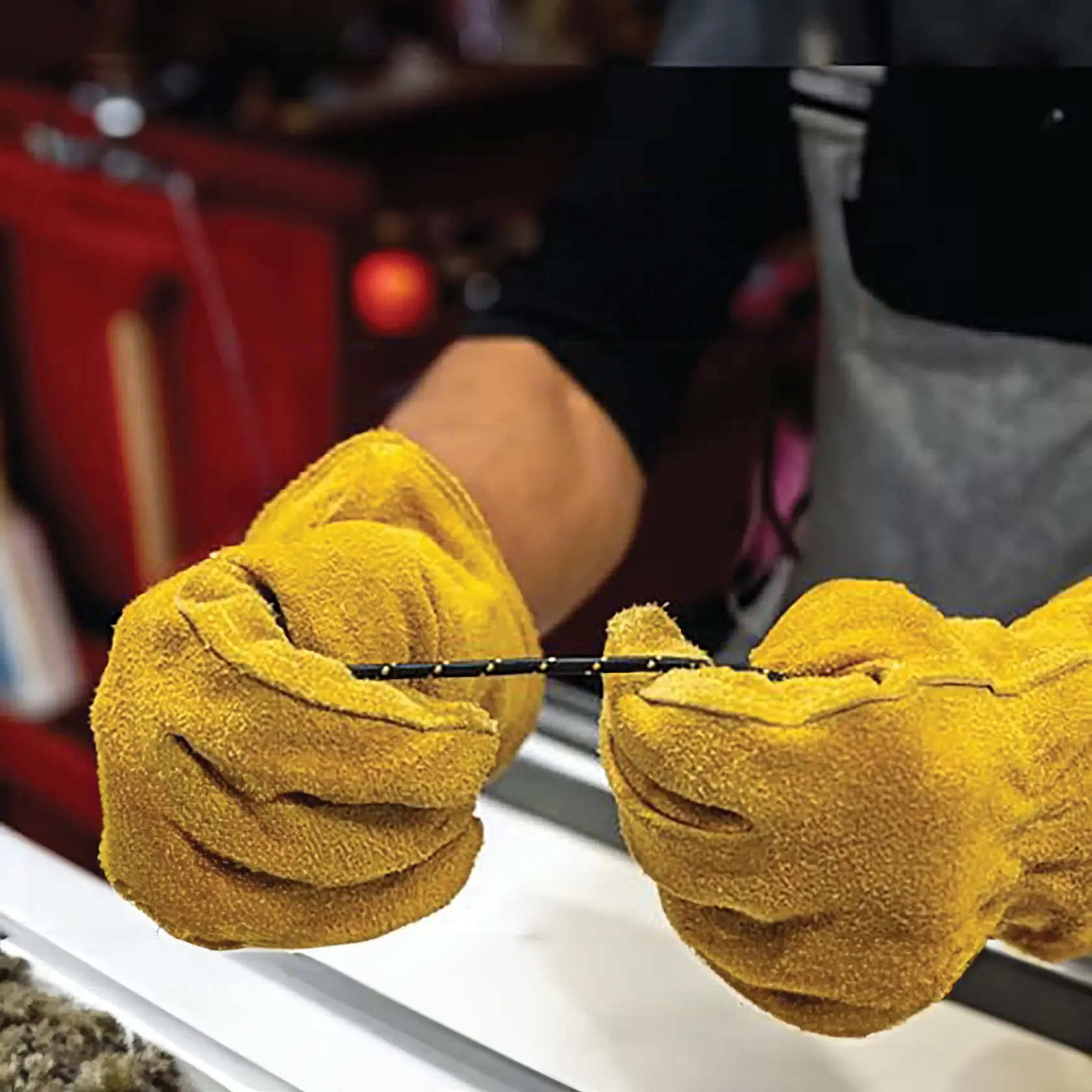 A person wearing large yellow work gloves holds a thin black cable, focusing on the hands and gloves.