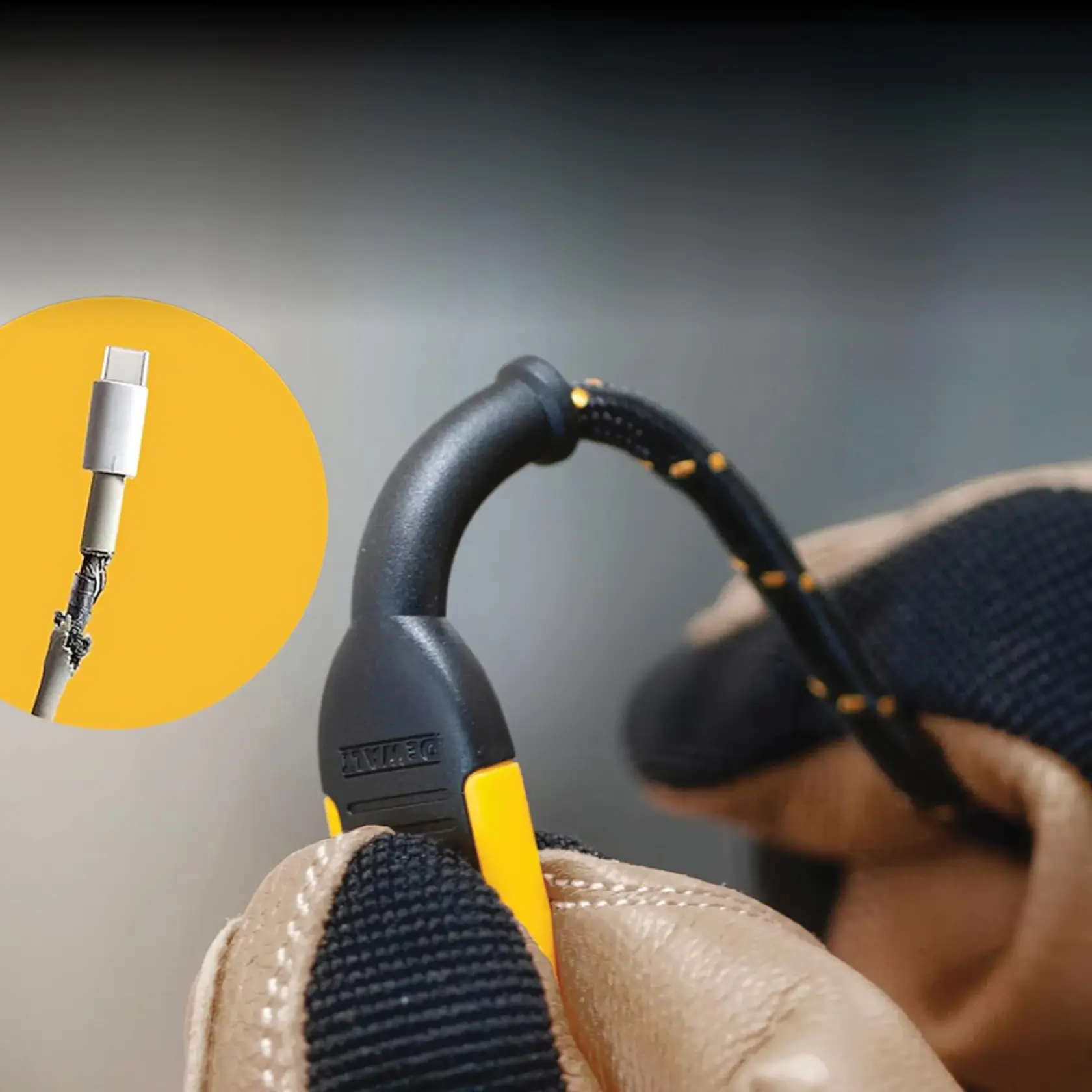 A close-up image of a DEWALT lanyard with a black and yellow design being held by a gloved hand. The lanyard is designed to secure a USB-C cable, highlighted in a yellow circle showing a frayed cable with a USB-C connector.