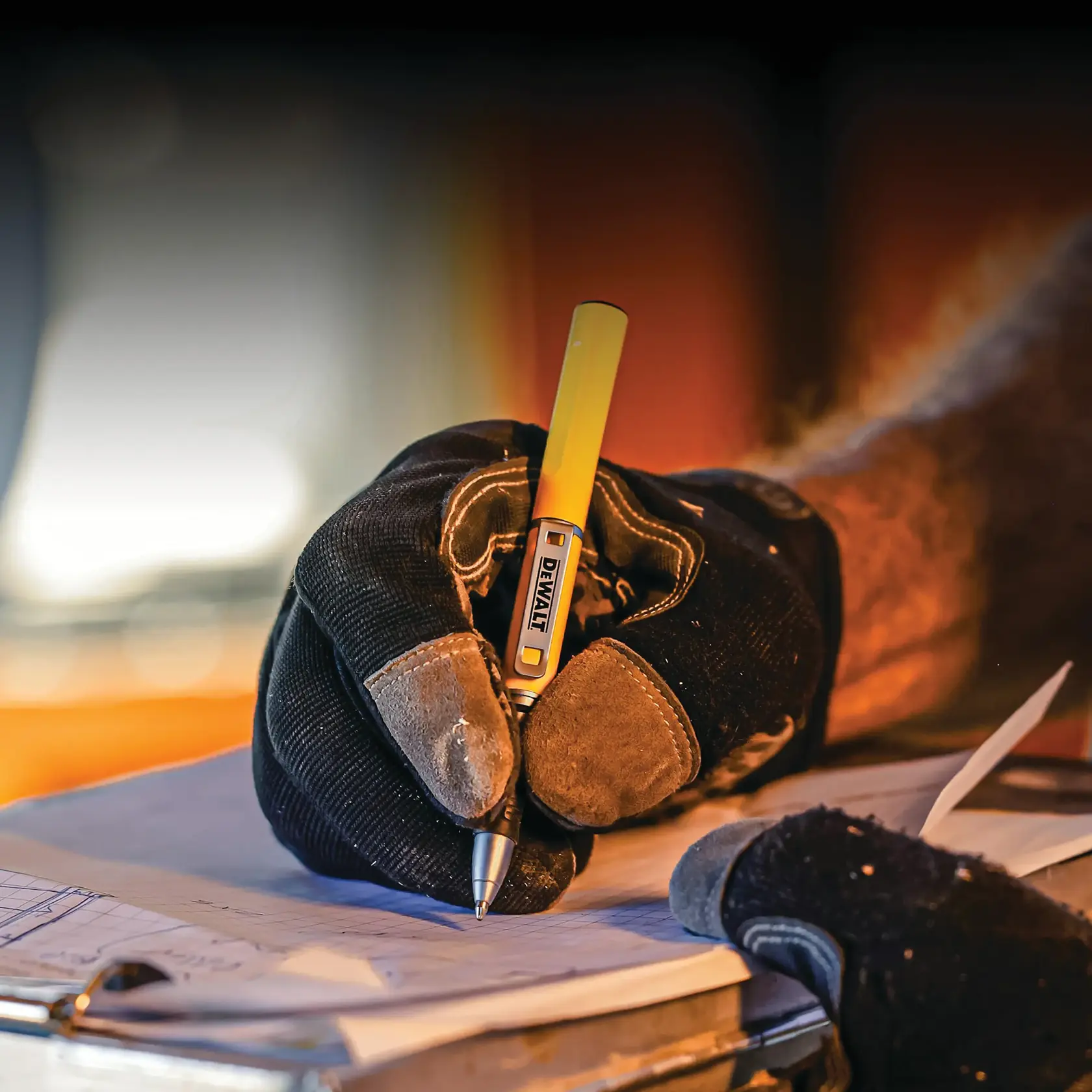 A person wearing work gloves is writing with a yellow DEWALT pen on a clipboard with paper. The environment suggests a professional or construction setting.