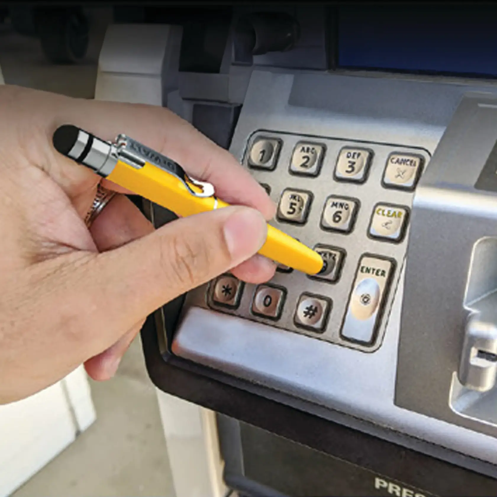 A person uses a yellow DEWALT stylus pen to press buttons on a keypad at a payment terminal, likely at a gas station.