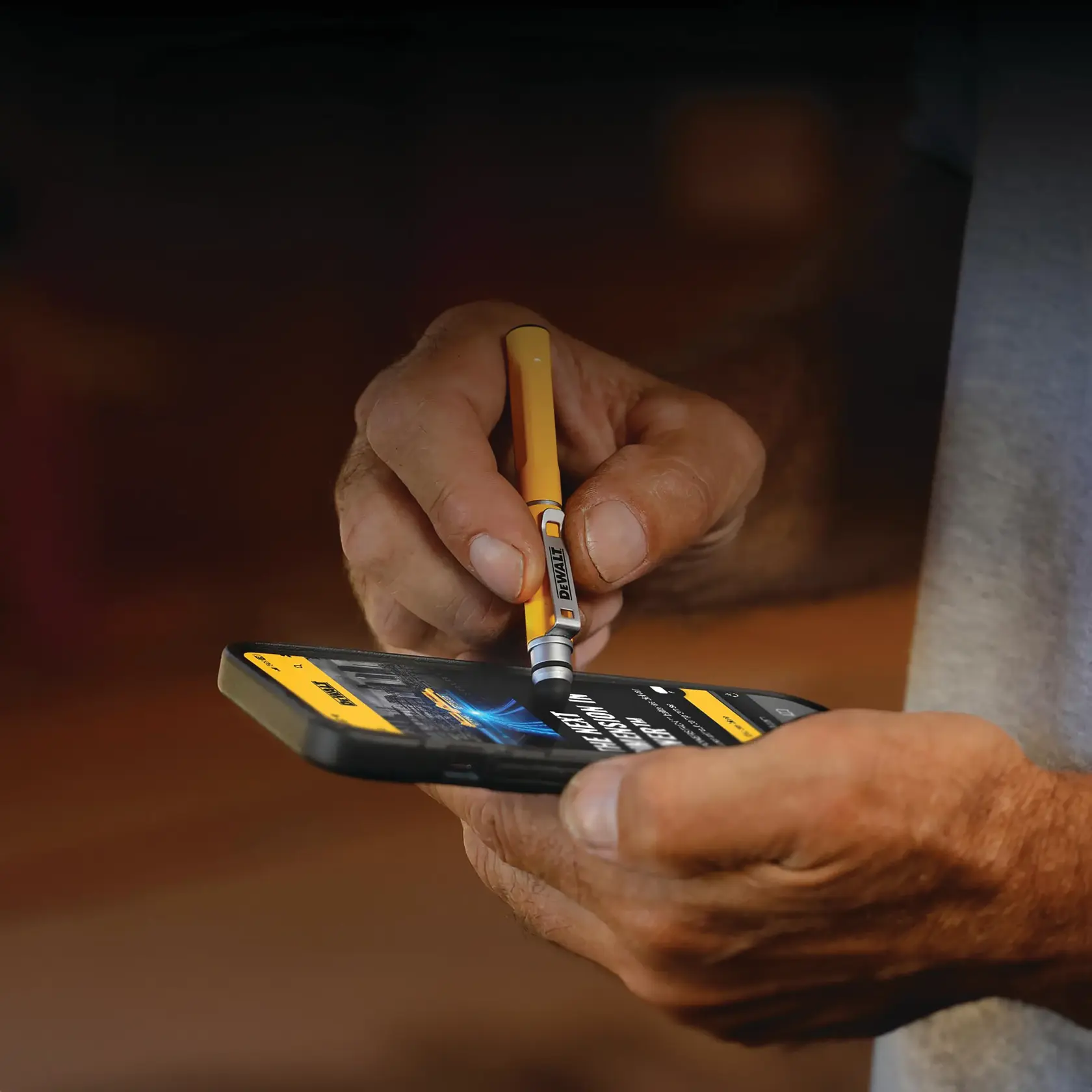 A person is using a yellow DEWALT stylus pen to interact with a smartphone screen.