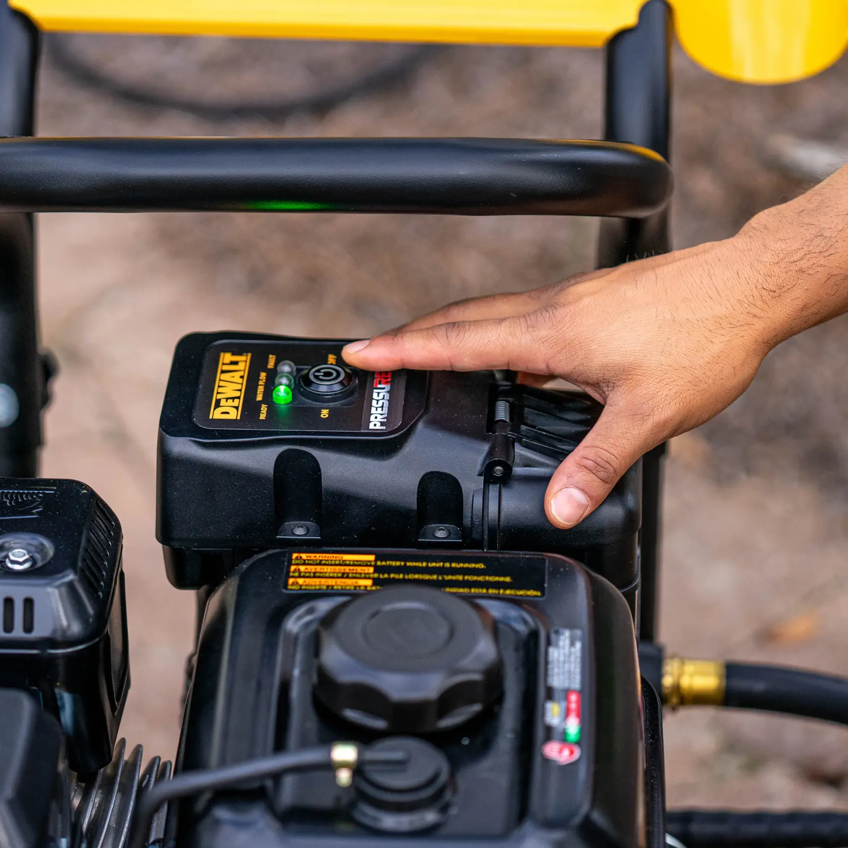 A close-up of a hand pressing the start button on a DEWALT pressure washer control panel outdoors.