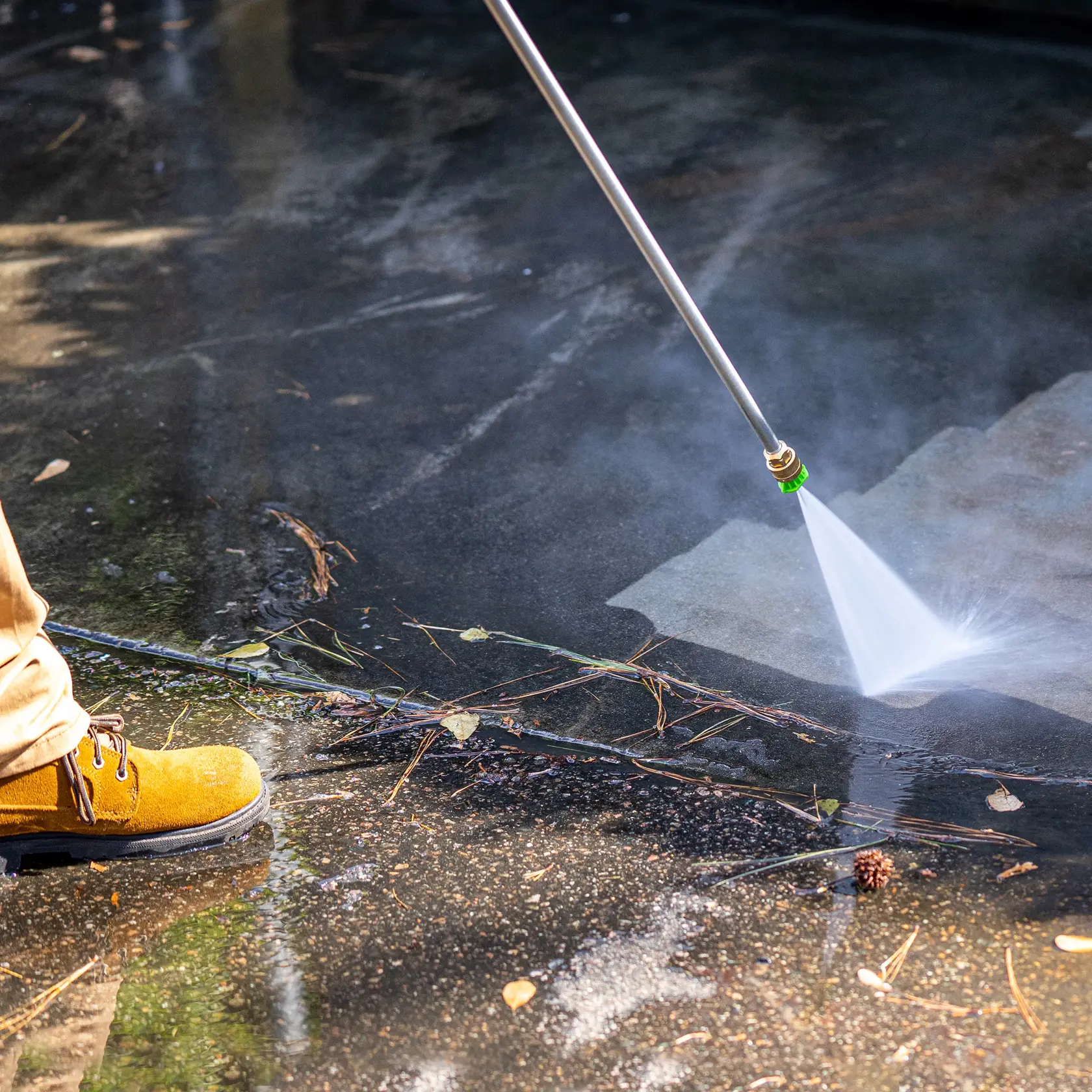 A person uses a pressure washer to clean a dirty outdoor surface, spraying water to remove debris and stains.